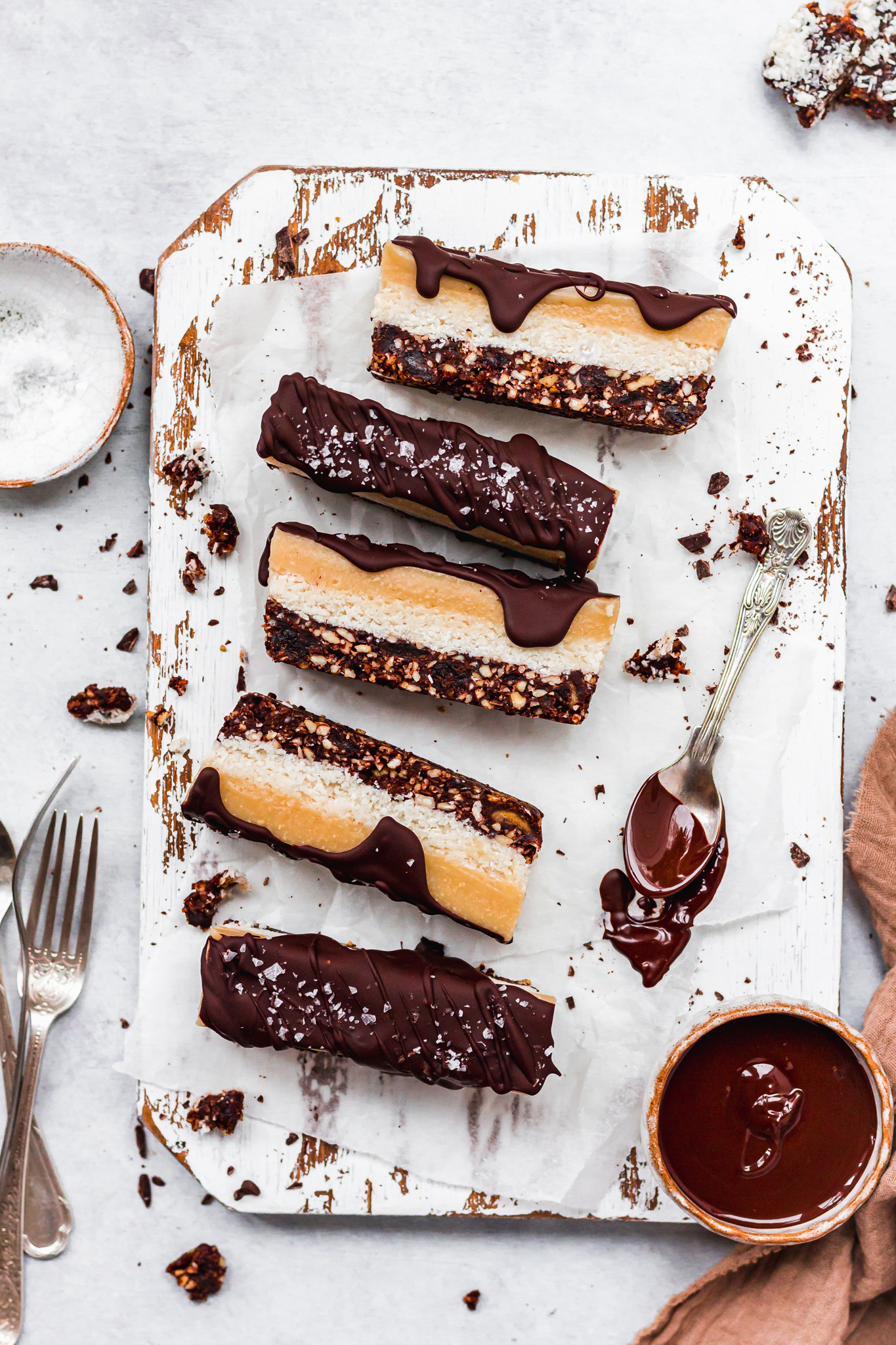 Salted Chocolate Coconut Caramel Slices on a white wooden board