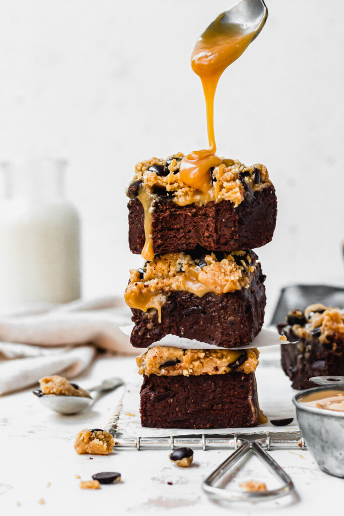 Drizzling caramel over a stack of No Bake Black Bean Brownie Cookie Dough Bars