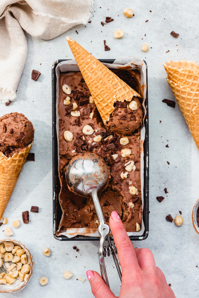 Taking a scoop from a tub of Double Chocolate Hazelnut Ice Cream (Vegan No-Churn)