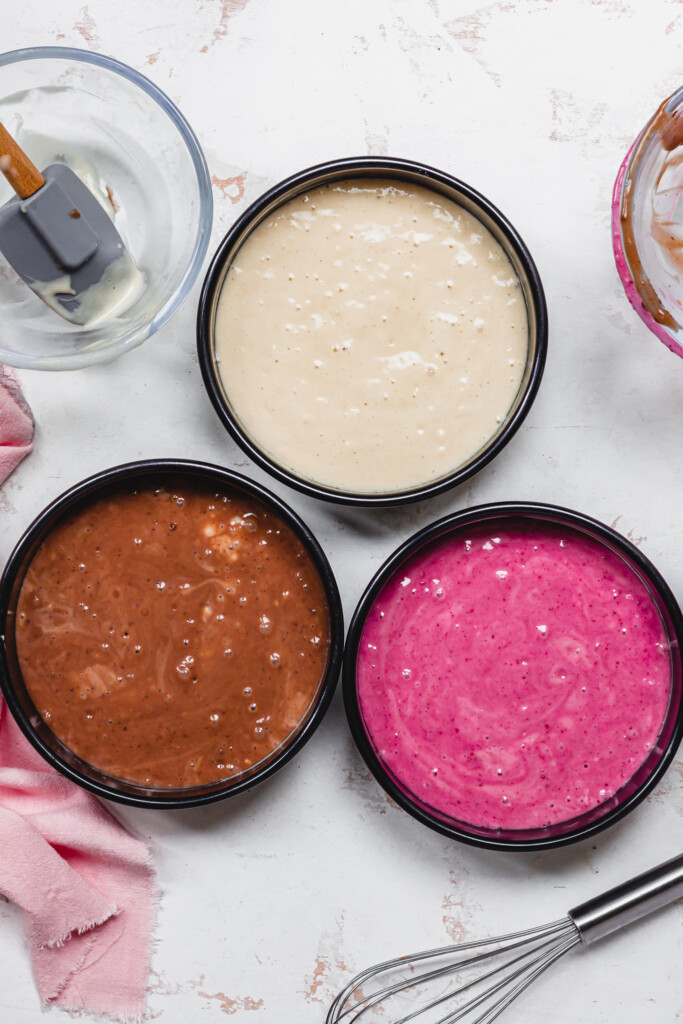 One strawberry, one chocolate and one vanilla cake batter in tins