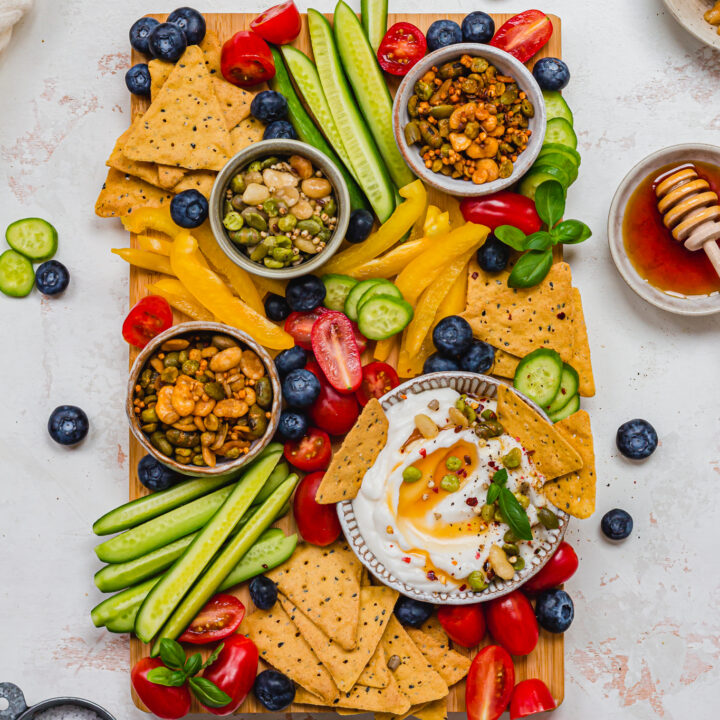 Wooden board covered with vegetables, crackers and a bowl of Vegan Garlic Whipped Feta