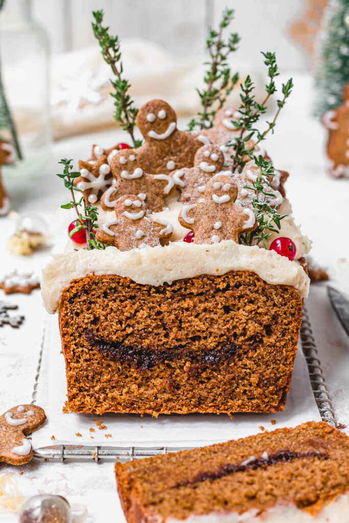 A slice of Vegan Gingerbread Loaf with Cream Cheese Frosting next to a loaf