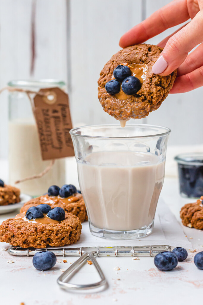 Dipping a Peanut Butter and Blueberry Breakfast Cookie into a glass of oat milk