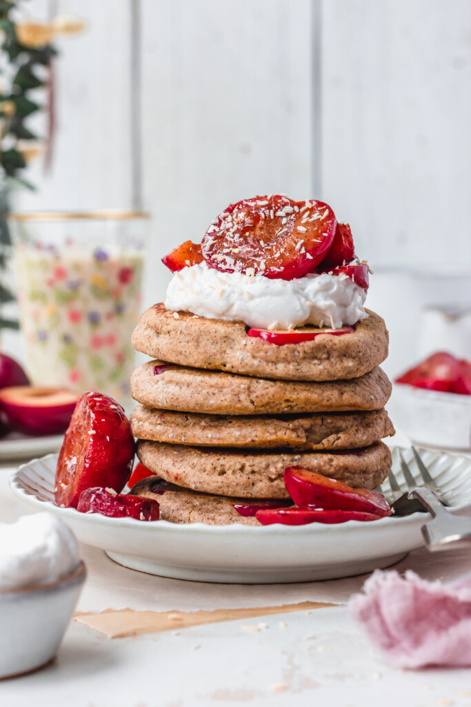 A stack of Sticky Maple Plum Pancakes topped with plums and yoghurt