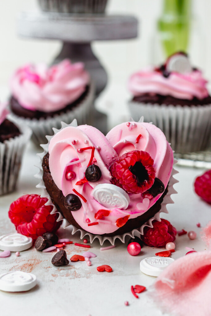 A heart-shaped cupcake with pink frosting and raspberries