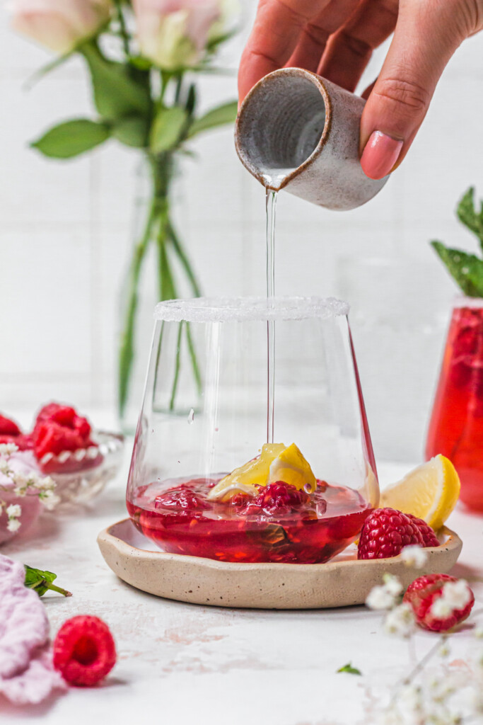 Pouring clear liquid into a glass of raspberries