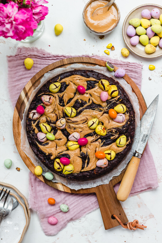 A round of Mini Egg Peanut Butter Flourless Brownies on a wooden board