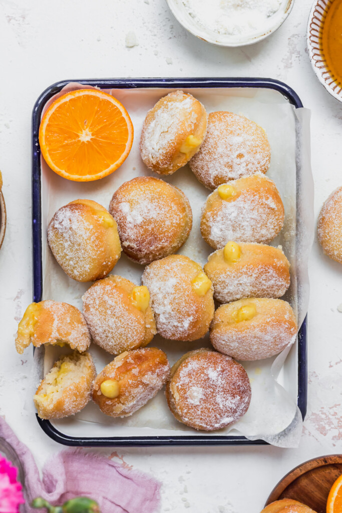 A white dish full of Orange Curd Air Fryer Baked Vegan Donuts with oranges