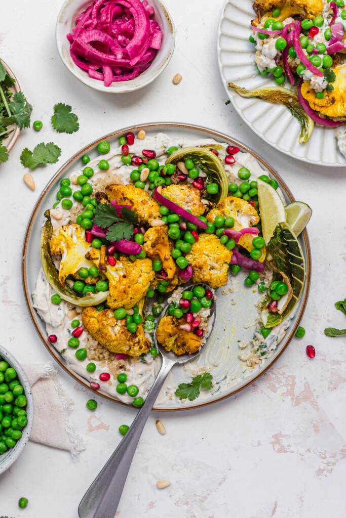 Half eaten plate of Roasted Cauliflower and Peas with Whipped Tahini with a spoon