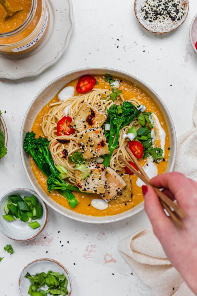 A hand and chopsticks over a bowl of Tofu Curry Ramen Noodles