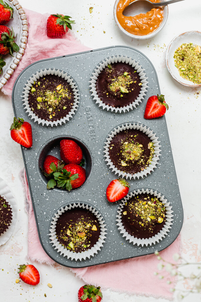 A six-hole muffin tray with chocolate cups and strawberries