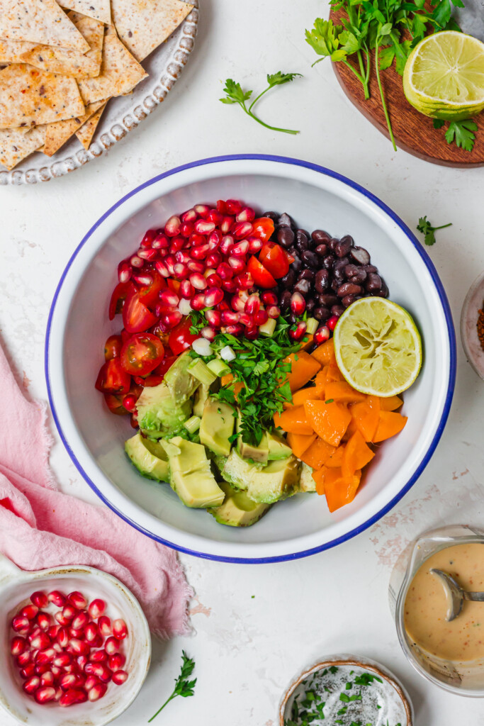 A bowl of salsa ingredients with pomegranate, tomatoes, black beans, lime, sugar mango and avocado