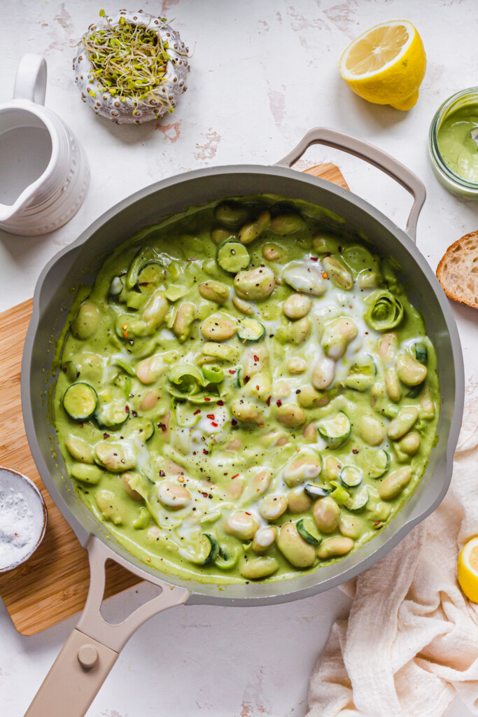 A pan of Creamy Pesto Butterbeans with lemon, herbs and a wooden board