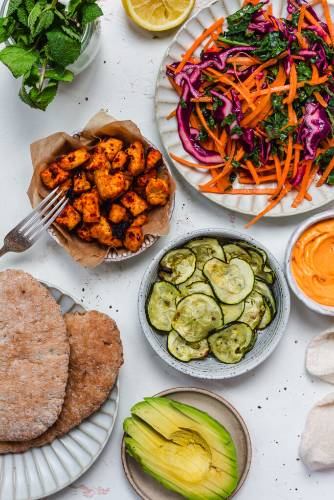 A bowl of slaw, a bowl of harissa tofu and courgettes with pitta bread and avocado