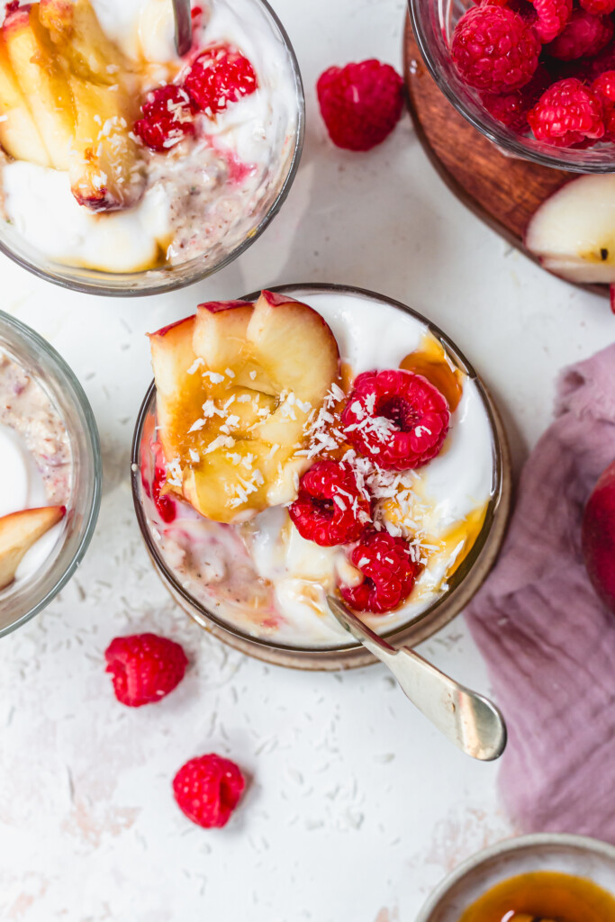 A spoon in a pot of Peach and Raspberry Creamy Oats with yoghurt and coconut flakes