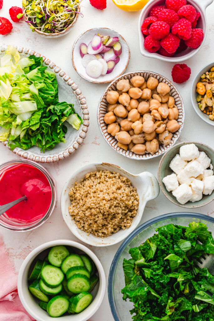 Ingredients in small bowls like chickpeas, raspberries, salad and quinoa