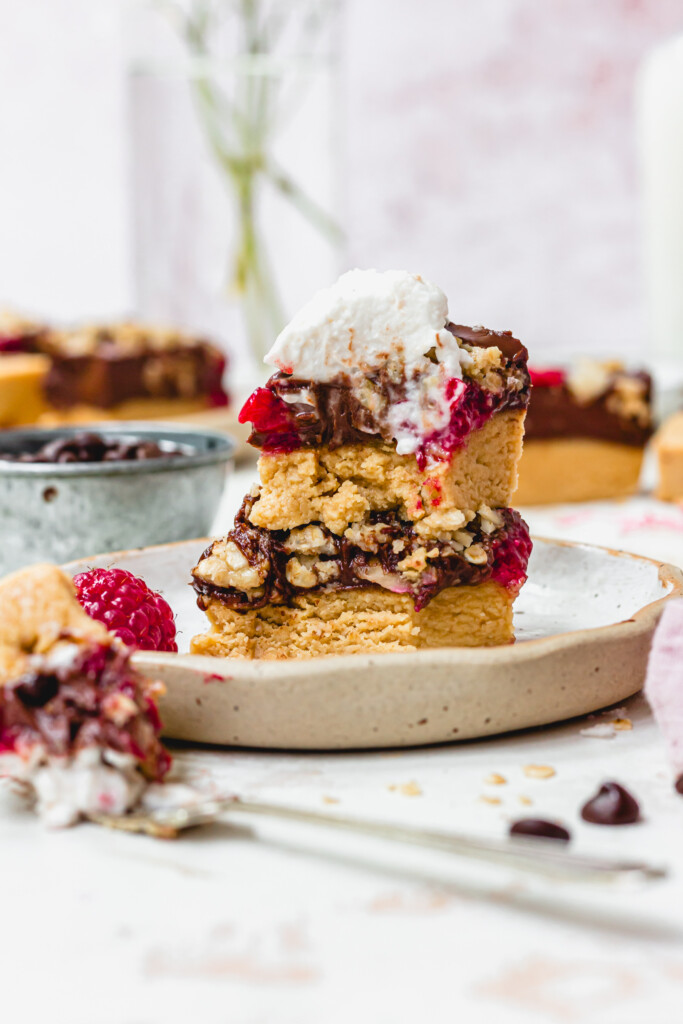 Two Chocolate Raspberry Ganache Crumble Bars on a plate with coconut cream