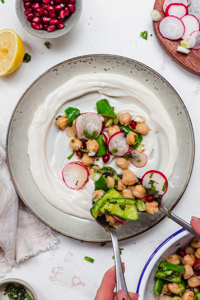 Spooning Smashed Cucumber and Chickpea Salad onto a plate of yoghurt