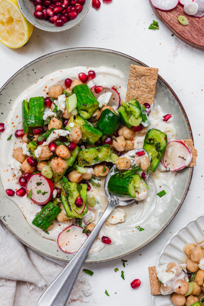 A spoon in a plate of yoghurt and Smashed Cucumber and Chickpea Salad
