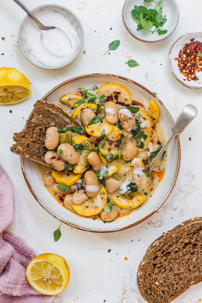 A bowl of Creamy Lemony Courgette Butterbeans with bread and a spoon