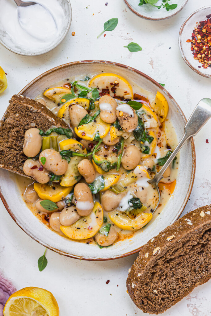 Close up of Creamy Lemony Courgette Butterbeans in a bowl with bread and a spoon