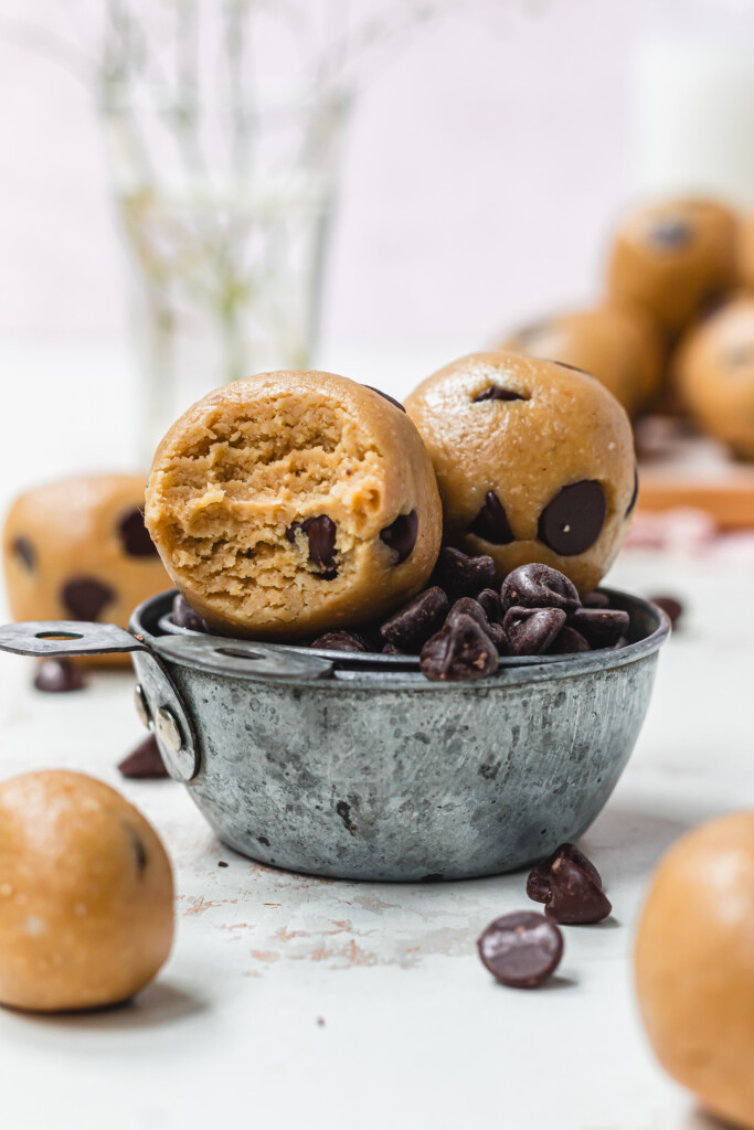 Two Healthy Chocolate Chip Cookie Dough Balls in a metal cup of chocolate chips