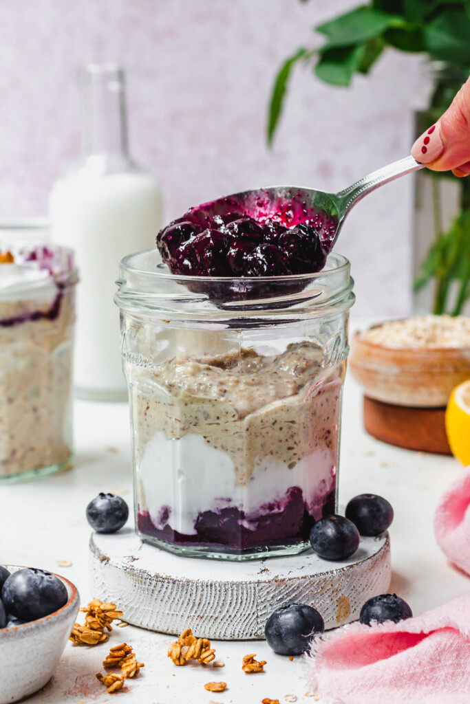 Spooning blueberry compote into a jar of oats and yoghurt