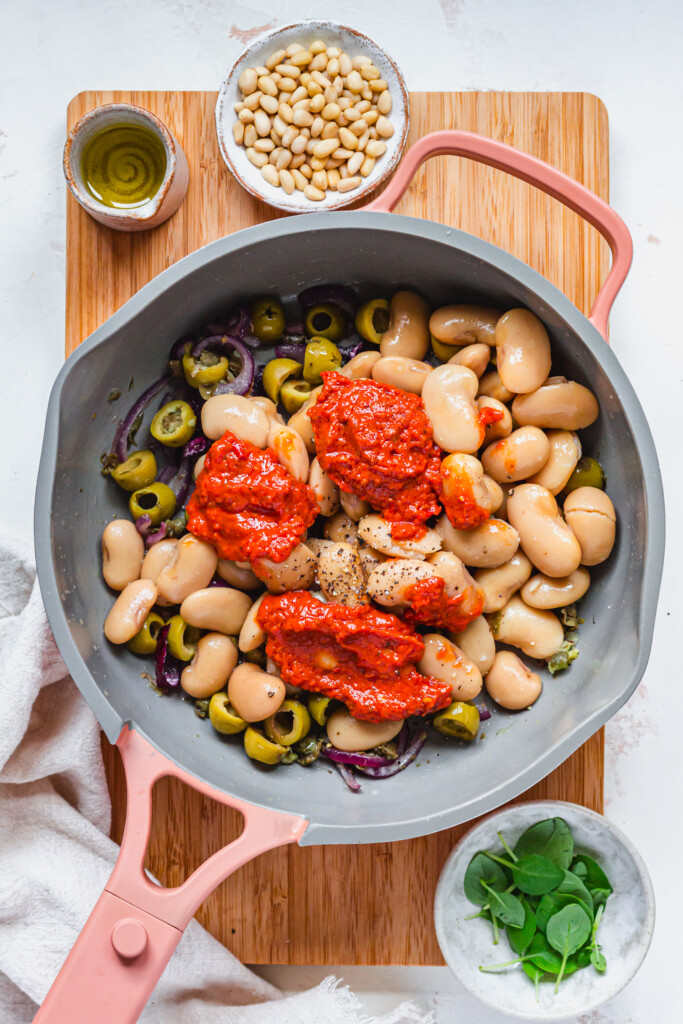A saucepan with beans, tomato pesto, olives and red onion