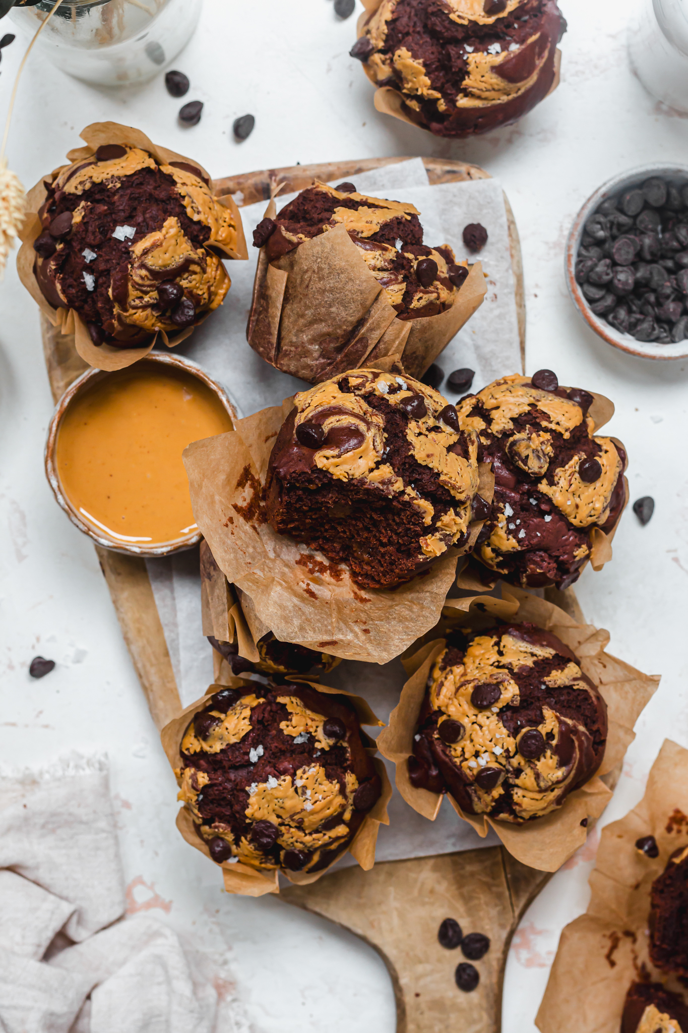 Some Bakery-Style Chocolate Peanut Butter Swirl Muffins with one bitten on a wooden board