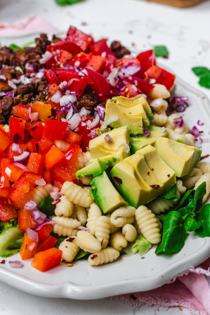 Close up of avocado, red pepper and black beans on pasta and salad