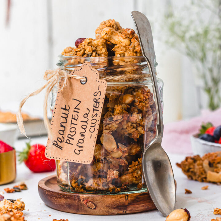 A jar of Peanut Butter Protein Granola Clusters with a spoon and label