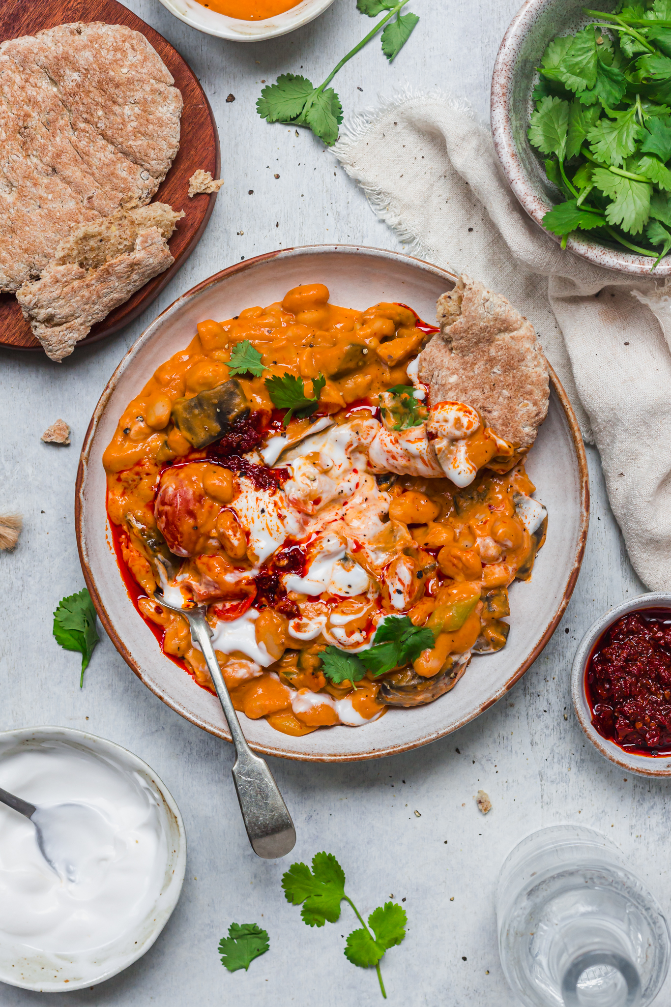 A bowl of Creamy Harissa Aubergine Beans with bread and a spoon