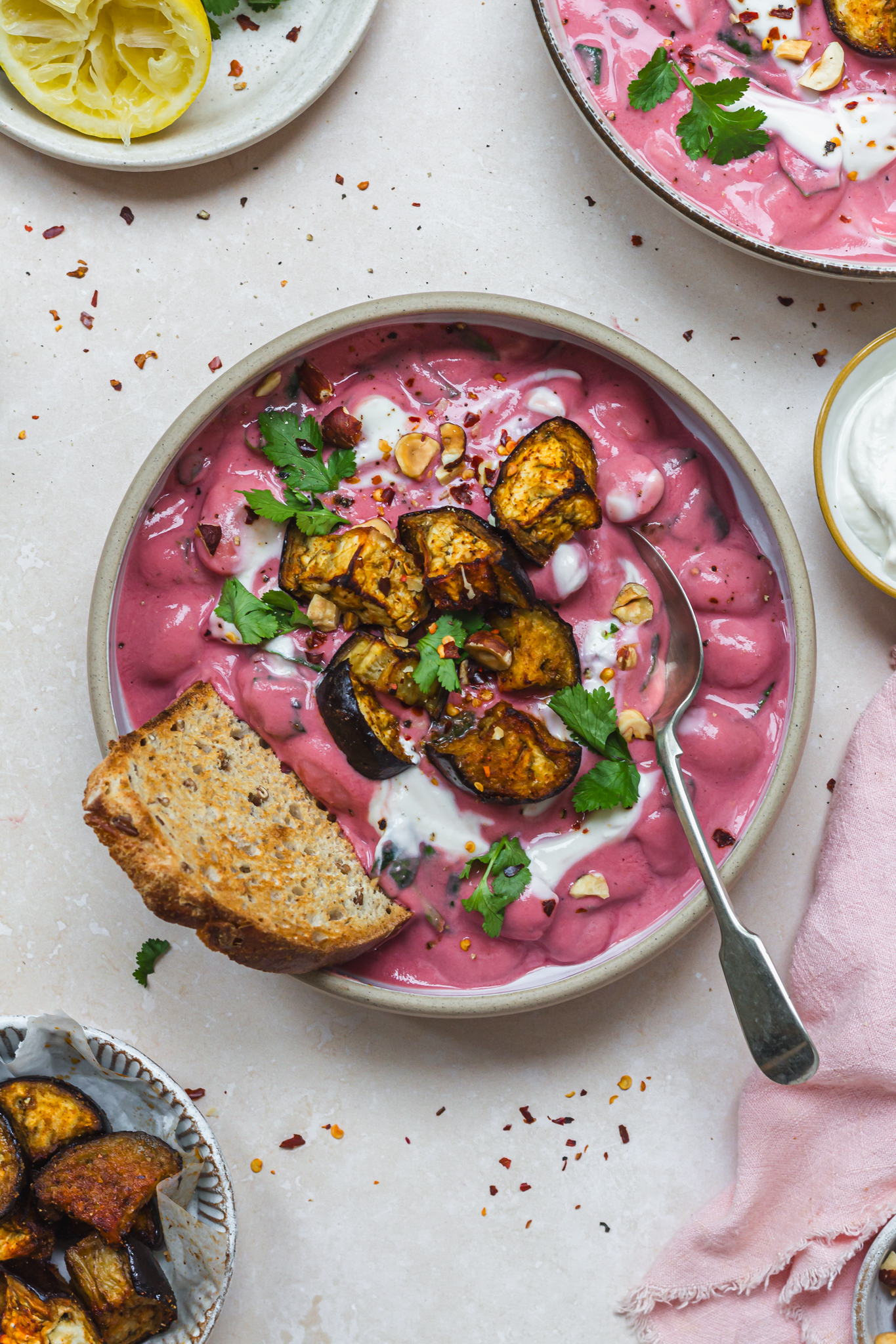 Close up of a bowl of Creamy Beetroot Miso Butterbeans with Roasted Aubergine with bread and a spoon